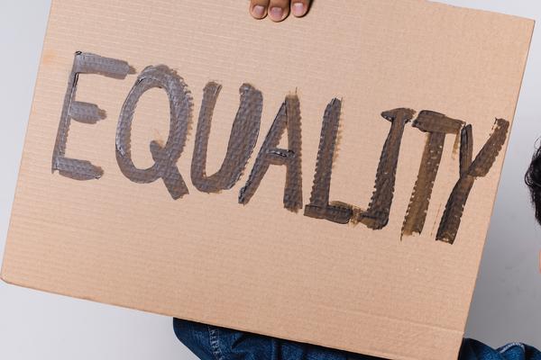 A person holding up a cardboard sign that says 'equality' on it in capital letters and black pen 