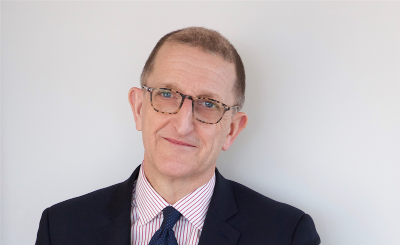 David Isaacs wearing glasses and a dark suit with red striped shirt