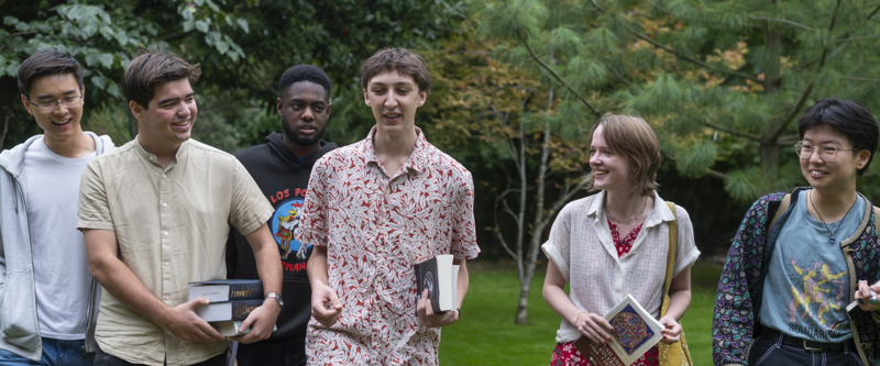A group of students carrying books and bags walk through Wadham College gardens talking 
