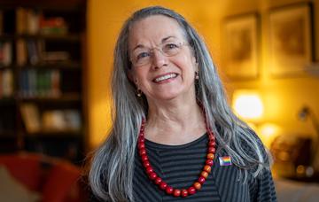Catherine Walter Catherine Walter in a warmly lit room wearing a charcoal and light grey top and big red beads