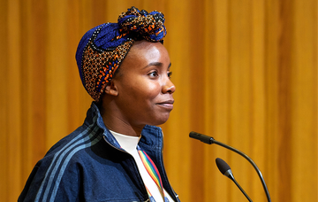 Vanessa Worthington standing at a lectern wearing a colourful blue and orange headscarf 