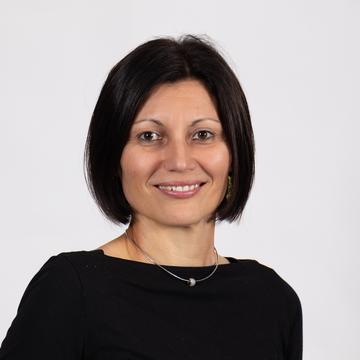 An image of Ivona Hideg wearing a black shirt and smiling against a plain white background. 
