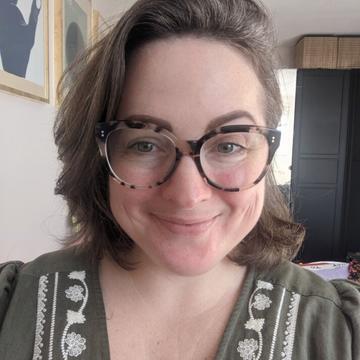 A head-and-shoulders photo of Katherine smiling, wearing glasses and a patterned green top.