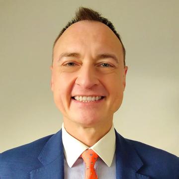 An image of Pavel wearing a blue suit and smiling against a plain background. 