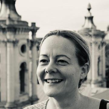 A black and white image of Sarah Lewis smiling against a backdrop of buildings. 