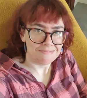 An image of Heather Stallard looking at the camera, wearing glasses and a pink and purple striped shirt. 
